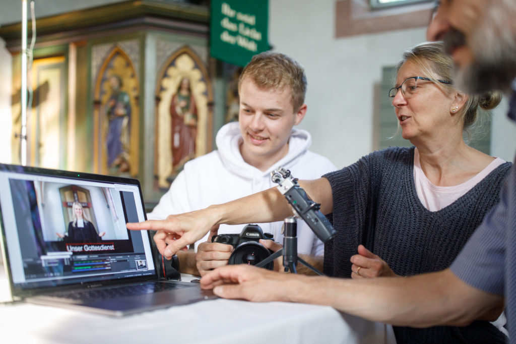 3 Personen sitzen vor einem Laptop und schauen sich einen Gottesdienst an.