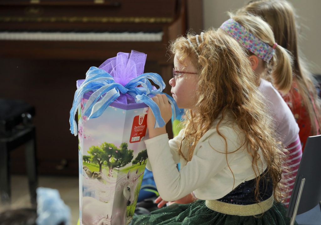 Mädchen sitzt in einer Kirche und hält eine große Zuckertüte fest, dahinter sitzen noch zwei weitere Kinder.